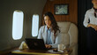 © Videophilia - Businesswoman focused on laptop aboard a private jet, working in luxury corporate travel while a flight attendant provides discreet service, symbolizing success and executive lifestyle