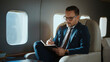 © Videophilia - Businessman in a suit and glasses writing in a notebook, concentrating on work while flying in a luxurious private jet, embodying success and exclusive travel