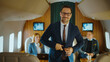 © Videophilia - Confident businessman smiling as he buttons his suit jacket inside a luxurious private jet cabin while colleagues work behind him, symbolizing executive travel and success