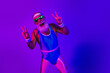 © deagreez - Retro fitness man in neon blue and purple jumpsuit dancing with peace signs under disco lights