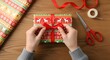 © Qii Stock - Hands tying a red ribbon bow around a wrapped Christmas gift, preparing for the holiday season.
