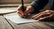 © HADI INCREDIBLE - Close-up of person signing a document on a wooden table with a pen.