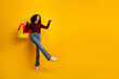© deagreez - Joyful young woman with shopping bags poses playfully against a bright yellow background promoting fashion shopping and style
