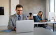 © NDABCREATIVITY - Young businessman using laptop computer in office. Manager thinks about successful financial ideas.