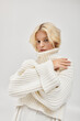 © LIGHTFIELD STUDIOS - Young blonde woman in cozy knitted sweater posing elegantly in a bright studio