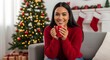 © Wool World - Smiling woman in a cozy red sweater holding a warm mug, radiating holiday cheer and comfort beside a festive Christmas tree at home