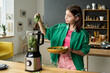 © Mediaphotos - Teenage girl preparing healthy smoothie by adding fresh spinach leaves into blender while standing in modern kitchen, holding bowl with ingredients, focused on cooking process