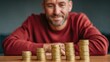 © ryker - Young man smiling while watching stacked coin pile growth on wooden table, financial planning concept, optimistic investment emotion