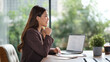 © wattana - Confident businesswoman smiling during an online meeting at her desk in a modern office.