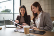© wattana - Two businesswomen happily discussing a report during a casual meeting in a modern workspace.