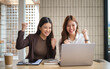 © wattana - Happy female coworkers cheering during an online meeting or achievement in a casual office setting.