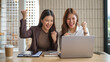 © wattana - Two excited businesswomen cheer in front of a laptop after a successful online result.