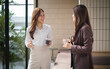 © wattana - Asian women in smart business attire enjoying a coffee and conversation in a bright, modern setting.