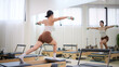 © wattana - Woman doing Pilates with dumbbells on a reformer, focusing on strength and balance.