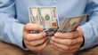 © Pavel - Close-up of male hands counting 100 US dollar bills. Man in blue shirt holding American currency. Financial concept background for income, salary or savings planning.