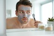 © Aliaksandr Barouski - Man applying a gray facial mask while looking in the mirror, focusing on skincare