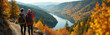 © miss irine - Two hikers with backpacks pause on a trail, taking photos of a vast valley with a river and colorful autumn trees. Couple enjoys scenic mountain landscape on a fall day. Explore nature on a walk.
