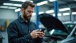 © miss irine - Bearded mechanic man uses modern smartphone gadget in auto repair service garage. Looks at mobile phone screen, thinking about complex car diagnostic issue. Pro guy solves technical problem, types on