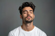 © miss irine - Portrait of young man with closed eyes. He has dark hair and beard. Man wears white t-shirt. Grey studio background. Attractive male model with stubble looks confident. He appears relaxed and calm.