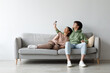 © Prostock-studio - Young Asian couple sits comfortably on a couch, using a remote control to adjust the split air conditioning system. They are relaxed and enjoying their time indoors together.