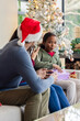 © Wavebreak Media - Family sitting on light sofa in living room beside Christmas tree unwrapping purple gift box