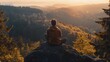 © Crafted - A man sits in a meditative pose on a rocky clifftop, looking out at a panoramic view of a valley covered in lush green forest with a misty sunrise in the distance.