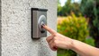 © Kilua - Close-up of a hand pressing a doorbell on a textured wall, with a blurred natural background