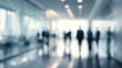 © morepiixel - A blurred scene featuring silhouettes of people in business attire walking through a modern, bright corridor.