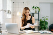 © Nuttapong punna - Smiling Asian woman standing and working with laptop in modern home office, concept of productivity, success, and female entrepreneurship.