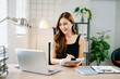 © Nuttapong punna - Smiling Asian woman standing and working with laptop in modern home office, concept of productivity, success, and female entrepreneurship.