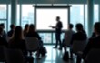 © Audrey - Abstract blur of modern office seminar, light streaming through glass windows, silhouettes of employees seated in rows, presenter mid-motion in front of projected slide. High quality