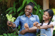 © Ekkasit A Siam - African woman teacher and asian preteen girl smiling together while proudly holding eggs in organic vegetable garden class during school farming activity outdoors with plants and baskets around