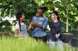 © Ekkasit A Siam - African female teacher showing young plant to asian preteen student and asian teenage girl during organic gardening class in school garden, engaging in hands-on farming lesson together outdoors