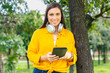 © Raquel - Happy woman wearing yellow shirt holding digital tablet and smiling outdoors in sunny green park,technology and lifestyle concept, natural background for design or promotional template