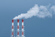 © SOLDATOOFF - Three industrial chimneys release thick white smoke into the blue sky, symbolizing air pollution and environmental impact.