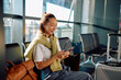© we.bond.creations - Asian woman traveler relaxing in airport departure lounge, holding passport and smartphone while waiting for boarding