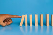 © Dadan - male hand drop wooden blocks isolated on blue background. domino effect or risk protection strategy concept
