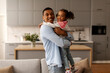 © Home-stock - Happy childhood. Cute black little girl embracing his loving daddy and smiling together to camera, posing at home in living room interior