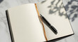© Moajjem - Blank open notebook with pen on white marble background and plant shadows