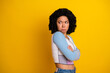 © deagreez - Young woman in casual attire against yellow backdrop displaying crossed arms and a thoughtful expression