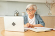 © Юлия Завалишина - Online education courses webinar concept. Middle aged senior woman using laptop computer writing notes. Focused mature old woman enjoying studying online from home written records doing online work