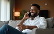 © Christopher - Happy businessman in hotel, on smartphone call and business communication for work in Atlanta. Young black entrepreneur, listening to audio on cellphone and sitting on luxury sofa in living room
