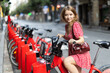© JackF - Young woman in red dress rents electric bike on street of european city