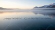 © Arsal Stock - Merry christmas message written on a frozen lake with mountains and fog in the background at sunrise creating a serene winter holiday scene