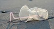 © Suryani - Discarded plastic cup and straw on sandy beach symbolizing environmental pollution