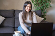 © VictorCanalesStudio - Woman smiling while typing on laptop during remote work on home couch with copy space