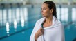 © Dara - A woman standing in an indoor swimming pool, wrapped in a white towel, with a calm expression on her face.
