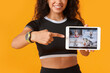 © Pixel-Shot - Sporty young African-American female coach pointing at tablet computer on yellow background. Concept of online training