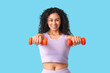 © Pixel-Shot - Sporty young African-American female coach with dumbbells on blue background