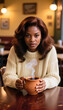 © deFusum - Young Black woman warming hands over steaming mug of coffee at café table